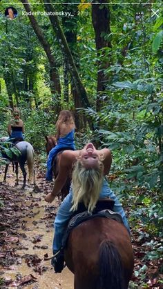 three people riding horses on a trail in the woods