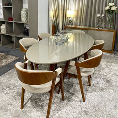 a dining table with six chairs and a vase on the side, in front of a bookshelf