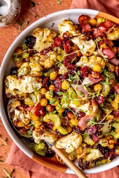 a bowl filled with lots of food on top of a red cloth next to a wooden spoon