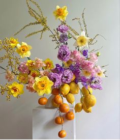 a vase filled with lots of different types of flowers and fruit on top of a white pedestal