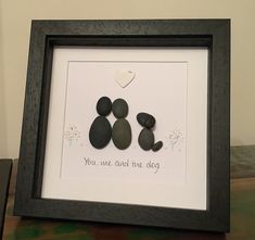 two pebbles in a black frame with a white heart on the wall behind them