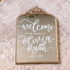 a welcome sign hanging from the side of a mirror on a tablecloth covered wall