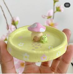 a hand holding a small toy mushroom on top of a yellow plate with flowers in the background