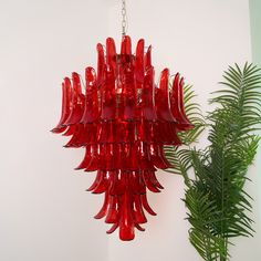 a red chandelier hanging from a ceiling next to a green plant in a room