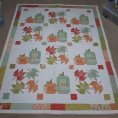 a quilted table topper with leaves and apples on it, sitting on the floor