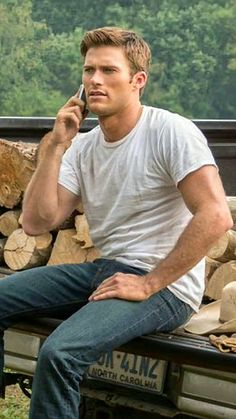 a man sitting on the back of a pick up truck talking on a cell phone