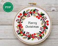 a cross - stitch christmas wreath with the words merry christmas on it is displayed in front of a wooden background