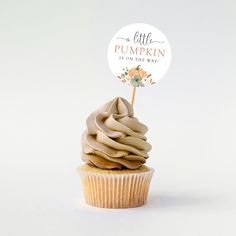 a cupcake with frosting sitting on top of a white table next to a sign that says little pumpkin is on the way