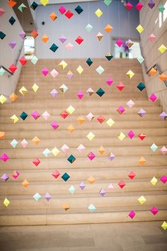 colorful paper cranes are hanging from the ceiling above some stairs in an office building with wooden steps