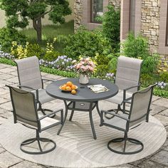 an outdoor dining set with four chairs and a table in front of some flowers on the ground