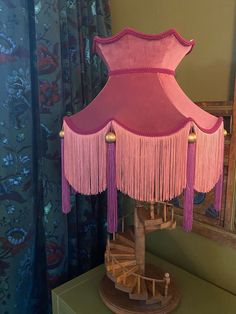 a pink lamp sitting on top of a wooden table next to a mirror and curtain