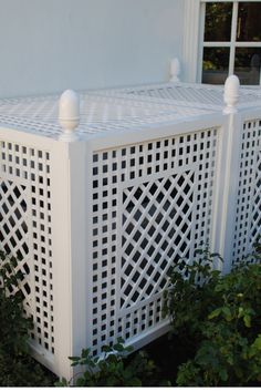 a white pergolated fence sitting in front of a window next to shrubbery