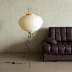 a brown leather couch sitting next to a white lamp on a stand in front of a wall