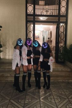 three girls wearing neon masks standing in front of an entrance to a building with stairs