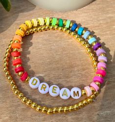 two bracelets with the word dream written in white and gold beads on a wooden table