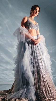 a woman in a silver and white dress standing on the beach with her arms around her waist