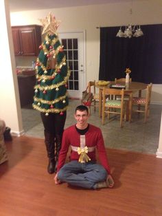 a man sitting on the floor in front of a christmas tree next to a woman