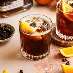 two glasses filled with iced tea and orange slices on a table next to coffee beans