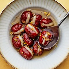 a white bowl filled with lots of food on top of a yellow table next to a spoon