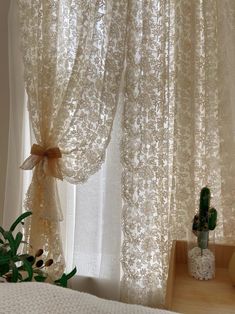 the curtains in this bedroom are white and have gold lace on them, along with a potted plant