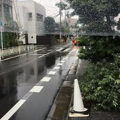 an empty street with rain falling on the ground and trees in the foreground behind it