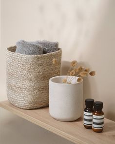 two bottles are sitting on a shelf next to a basket with towels and some flowers