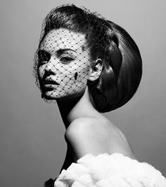 a woman with makeup and veil on her head wearing a white feathered dress in front of a gray background