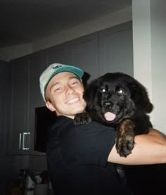 a man is holding a black dog in his arms and smiling at the camera while wearing a hat