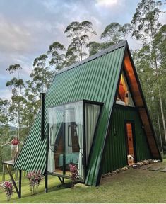 a green house with a metal roof in the middle of some grass and trees around it