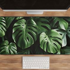 a computer desk with a keyboard, mouse and green leaves on the wall behind it