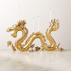 a golden dragon candle holder sitting on top of a white table next to three candles