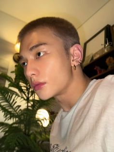 a young man with ear piercings standing in front of a plant