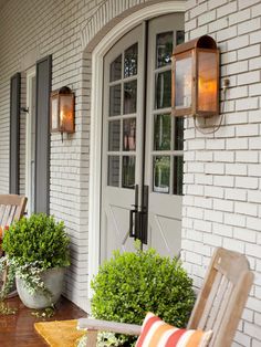 a porch with chairs and potted plants on the front steps, next to an open door