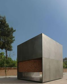 a large metal structure sitting on top of a cement floor next to a tree and building