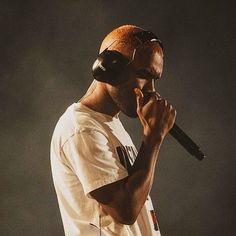 a man with headphones on holding a microphone to his ear while standing in front of a dark background