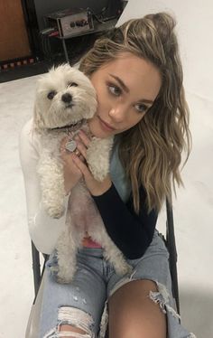 a woman sitting in a chair holding a white dog