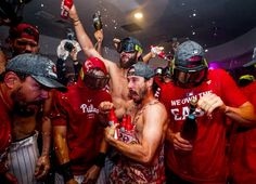 a group of men in red shirts holding bottles and wearing baseball caps with their hands up