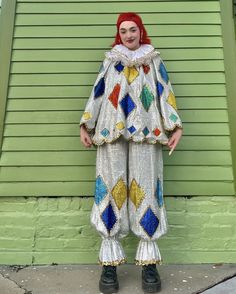 a woman dressed as a clown standing in front of a green building with a red head