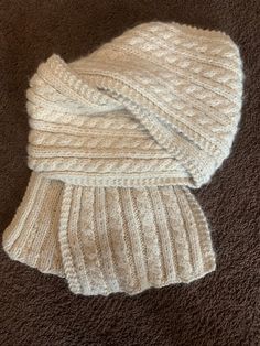 a white knitted hat and scarf laying on the floor in front of a brown carpet