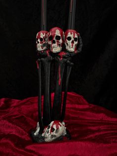 three red and black skulls are in the middle of two tall candles on a red cloth