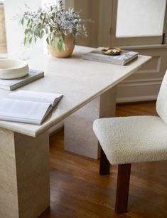 a desk with a book, pen and flower pot on it in front of a window