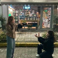 two women sitting on the ground in front of a store with their hands up to each other