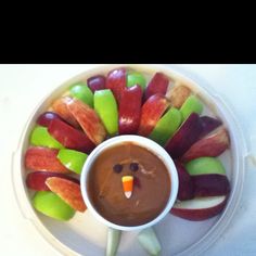 a white plate topped with candy apples and fruit shaped like a turkey next to a cup of chocolate