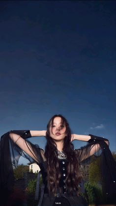 a woman with long hair wearing black clothes and holding her arms behind her head while posing for the camera