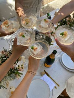 several people are holding wine glasses over a table with plates and flowers on it,