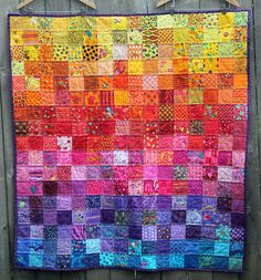 a colorful quilt hanging on the side of a wooden fence with clothes pins attached to it