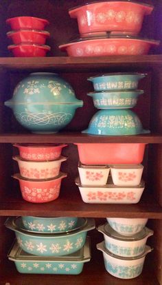 many different colored dishes are stacked on top of each other in a wooden cabinet with glass lids