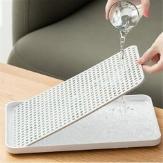 a person pouring water into a glass on top of a white tray next to a green chair