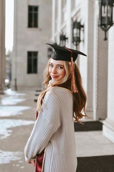 a woman wearing a graduation cap and gown standing in front of a building with columns