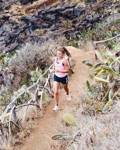 a woman is running down a trail in the desert with cactus and rocks behind her